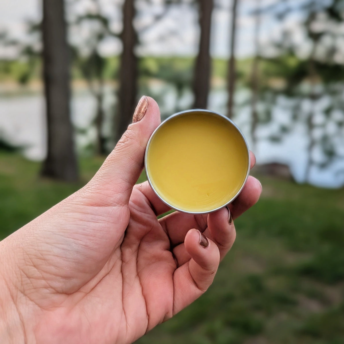 Hand holding an open tin of Wyldflower Apothecary organic healing salve